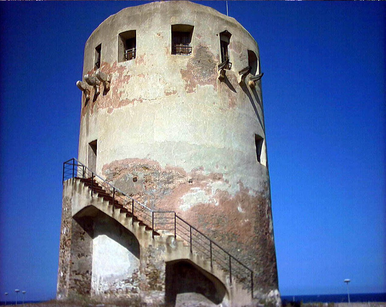Torre costiera cilindrica di Porto Corallo con scala esterna sotto un cielo blu