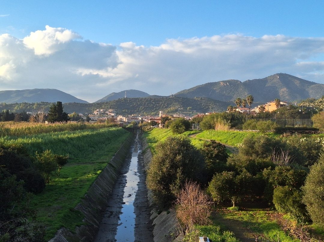 Veduta di Villaputzu con campi verdi, un canale e le montagne del Sarrabus sullo sfondo